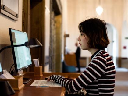 A student sitting at a desktop computer. They are wearing a stripy jumper.