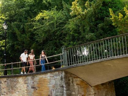 3 people walking along a stone bridge. There are railings in front of them and trees behind them. 