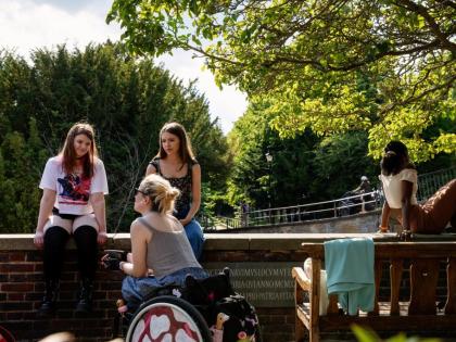 A group of students siting on a wall. One is in a wheelchair. There is a tree above them. 