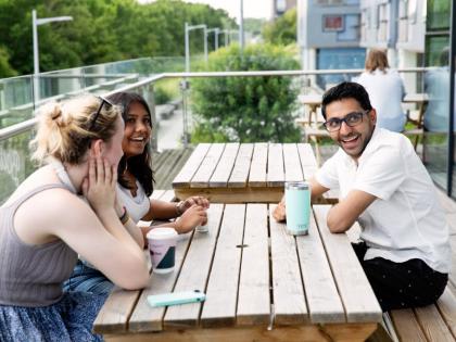 £ people sitting at a picnic table. They are smiling and laughing and drinking.