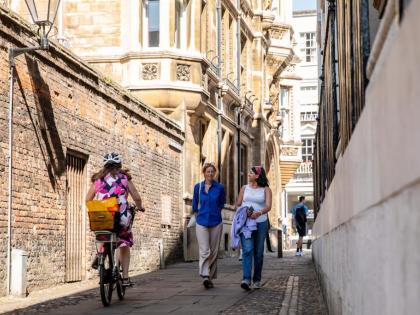 2 people are walking down an alley between two buildings. There is another person on a bike. 