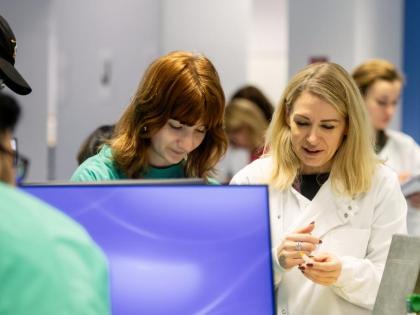 2 people in lab coats. They are working in a computer. In the foreground there is a blank computer screen.