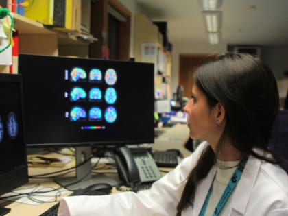 A doctor with their hand on the keyboard and looking at a screen that has brain images on it. 